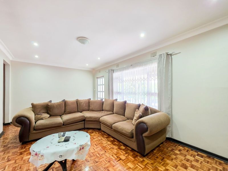 A living room featuring classic parquet flooring, recessed downlighting, and a security gate over the window, providing a functional and well-lit space.