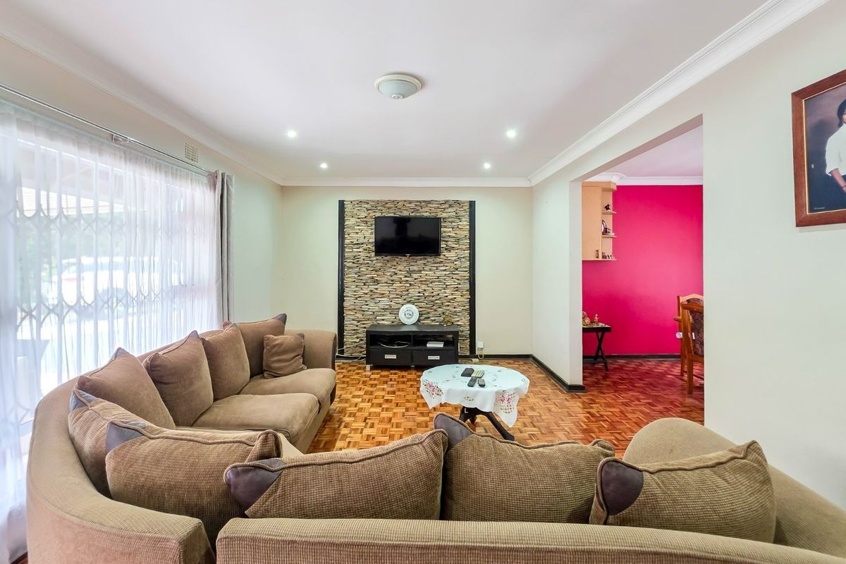 A spacious living room featuring parquet flooring, a stone-clad feature wall, and recessed lighting, with an open-plan flow into the adjacent dining area.
