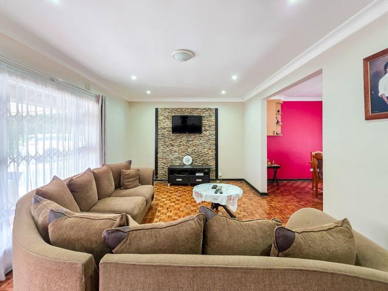 A spacious living room featuring parquet flooring, a stone-clad feature wall, and recessed lighting, with an open-plan flow into the adjacent dining area.