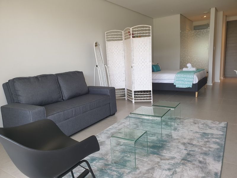 An open-plan studio apartment featuring neutral tiled flooring, recessed lighting, and a modern frosted glass partition separating the sleeping area.