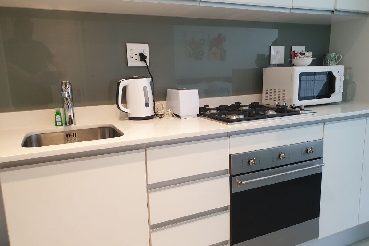 Modern kitchen featuring white cabinetry, stone countertops, a glass splashback, stainless steel sink, and integrated gas hob with built-in oven.