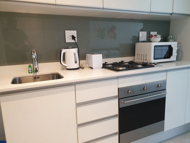 Modern kitchen featuring white cabinetry, stone countertops, a glass splashback, stainless steel sink, and integrated gas hob with built-in oven.