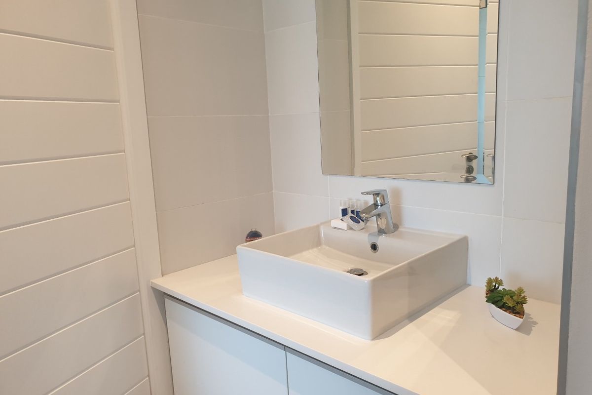 A modern bathroom vanity featuring a white vessel sink, chrome mixer tap, and a clean tiled wall finish.