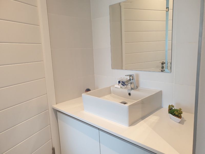 A modern bathroom vanity featuring a white vessel sink, chrome mixer tap, and a clean tiled wall finish.