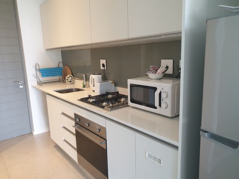 Modern galley-style kitchen featuring white cabinetry, stone countertops, a gas hob, built-in oven, and a sleek glass splashback.