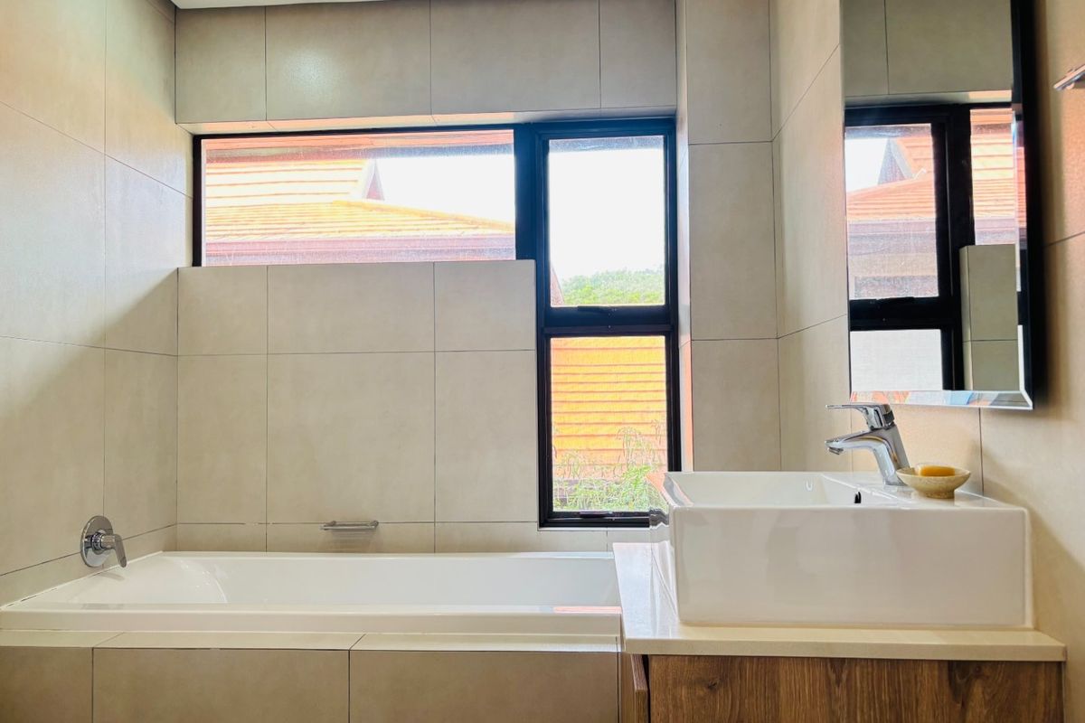 Modern bathroom featuring a built-in bathtub, a vessel sink on a wooden vanity cabinet, and large format wall tiles with a window.