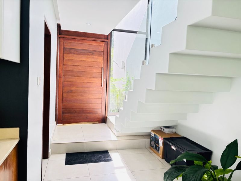 Modern entrance hall featuring a striking floating staircase with glass balustrade and a solid timber front door, finished with clean tiled flooring.