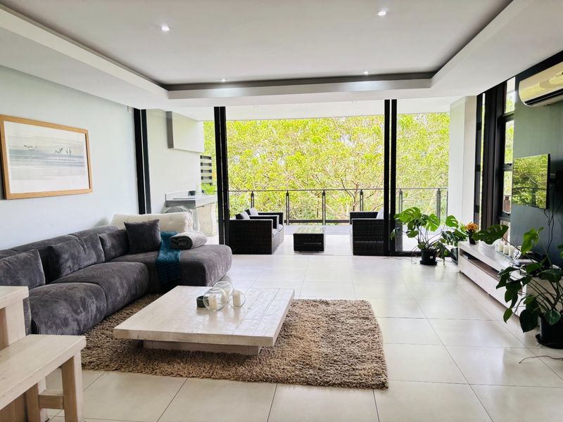 Spacious open-plan living area featuring modern tiled floors, recessed lighting, and large sliding doors that open onto a covered patio with a built-in braai.