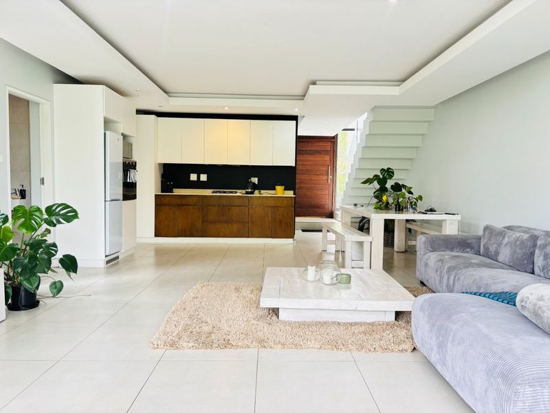 Spacious open-plan living area featuring a modern kitchen with two-tone cabinetry, tiled flooring, and a staircase leading to the upper level.