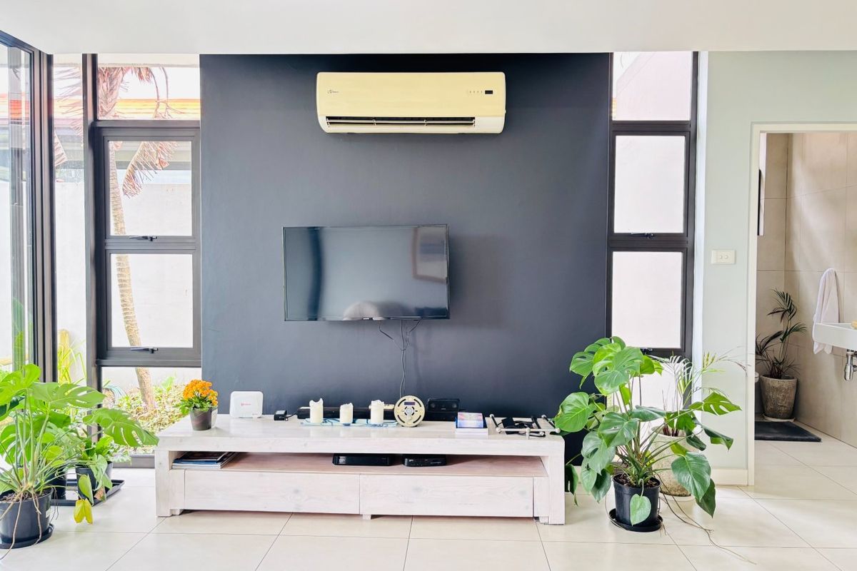 A bright living room featuring a dark accent wall, split-system air conditioning, and large windows providing natural light and garden views.