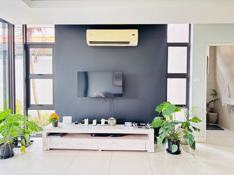 A bright living room featuring a dark accent wall, split-system air conditioning, and large windows providing natural light and garden views.