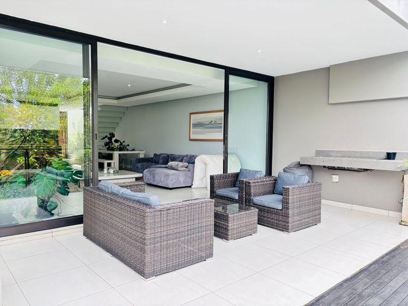 Covered patio featuring tiled flooring, recessed lighting, and a built-in braai, with large sliding glass doors providing seamless access to the interior living area.