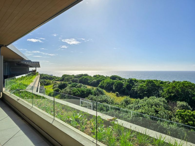Spacious penthouse balcony featuring a modern glass balustrade, integrated planter box, and expansive panoramic ocean views.