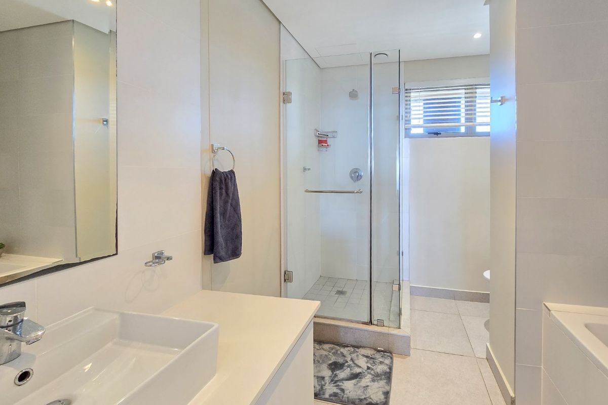 Modern bathroom featuring a sleek vanity basin, glass-enclosed shower, and a built-in bathtub with neutral tiling throughout.