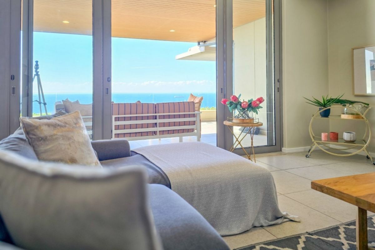 Bright living room featuring large sliding glass doors that open onto a spacious balcony with expansive ocean views.