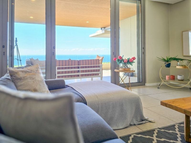 Bright living room featuring large sliding glass doors that open onto a spacious balcony with expansive ocean views.