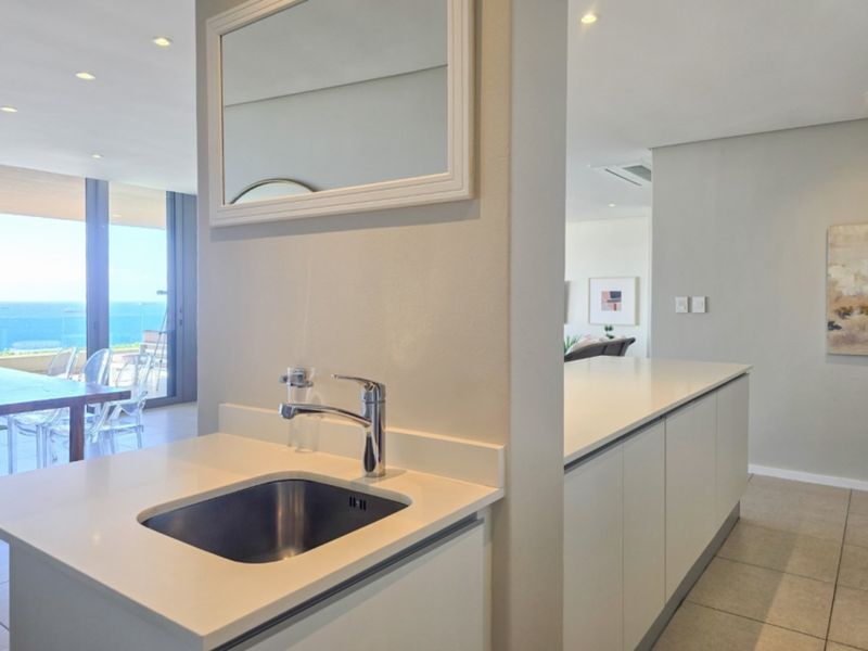 A modern, minimalist scullery area featuring a sleek undermount sink, chrome mixer tap, and stone countertops, seamlessly integrated into the open-plan penthouse layout.