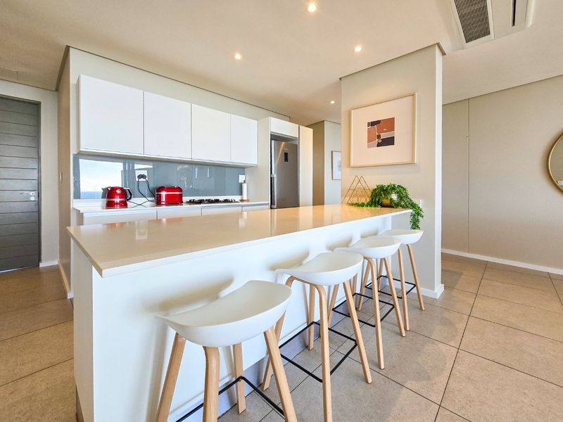 Modern kitchen featuring a large quartz island, sleek white cabinetry, integrated appliances, and recessed lighting, creating a clean and functional open-plan space.