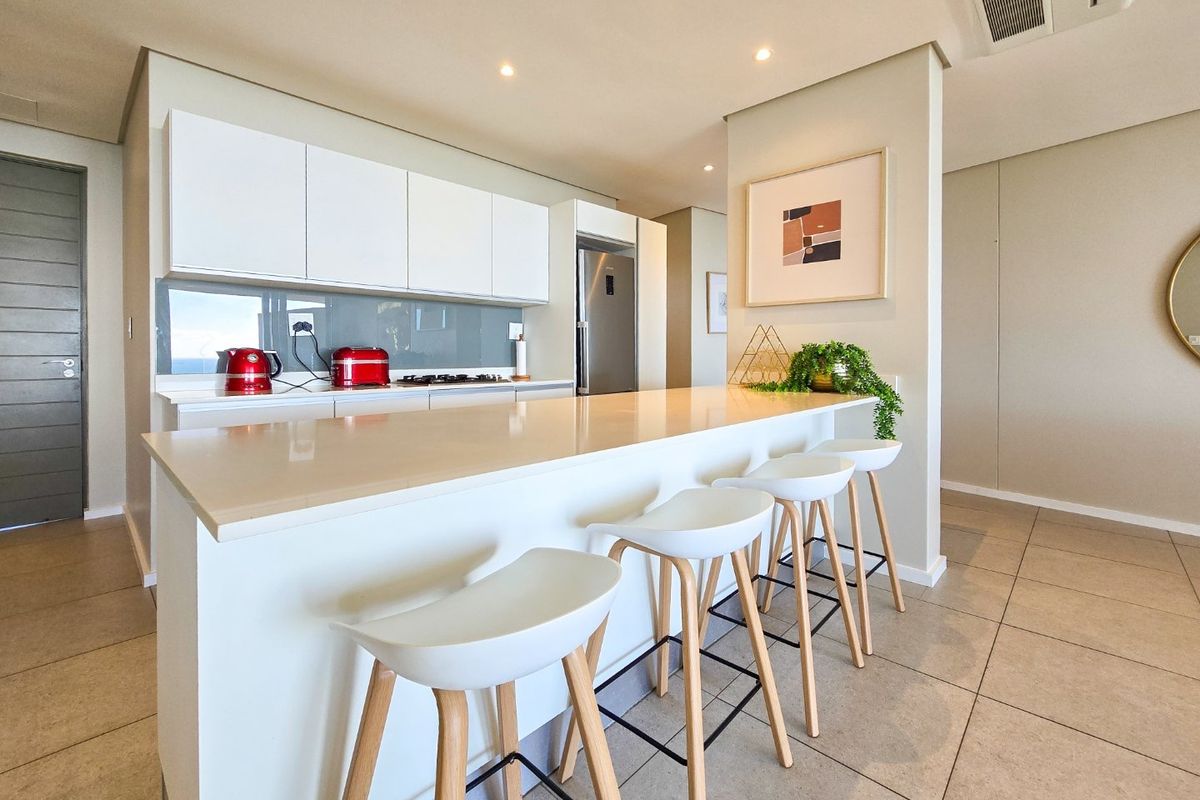 Modern kitchen featuring a large quartz island, sleek white cabinetry, integrated appliances, and recessed lighting, creating a clean and functional open-plan space.
