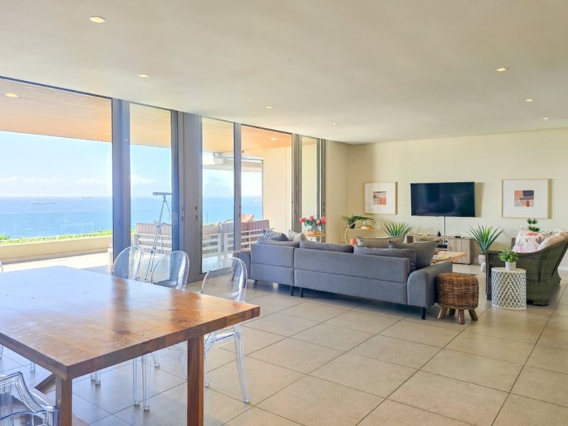 Spacious open-plan living and dining area featuring large format floor tiles, recessed lighting, and expansive floor-to-ceiling sliding doors opening onto a scenic balcony.