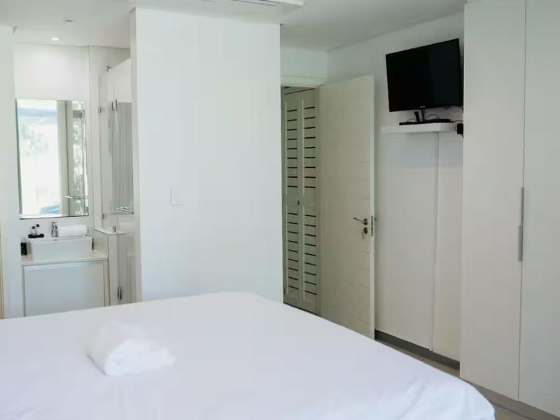 A clean, modern bedroom featuring a built-in wardrobe and an integrated en-suite bathroom with a vanity basin.