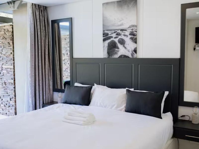 A well-appointed bedroom featuring a dark custom headboard, integrated bedside tables, and a striking stone feature wall with modern recessed lighting.