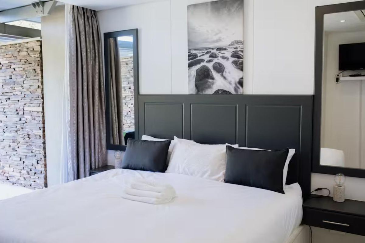 A well-appointed bedroom featuring a dark custom headboard, integrated bedside tables, and a striking stone feature wall with modern recessed lighting.