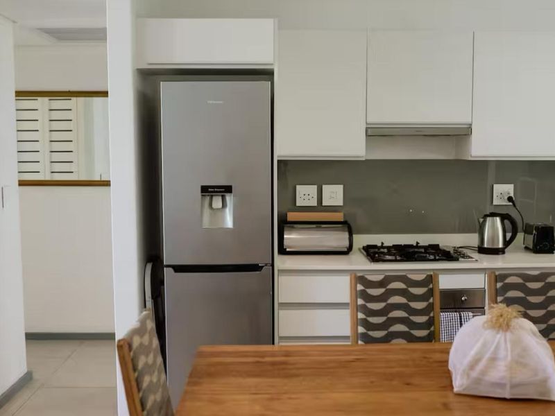 Modern kitchen featuring white cabinetry, gas hob, under-counter oven, extractor fan, and sleek glass splashback, seamlessly integrated with the dining area.