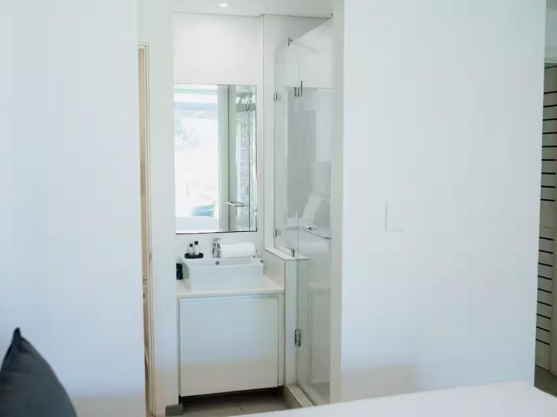 A clean, modern bathroom featuring a white vanity with a vessel sink, wall mirror, and a glass-enclosed shower.