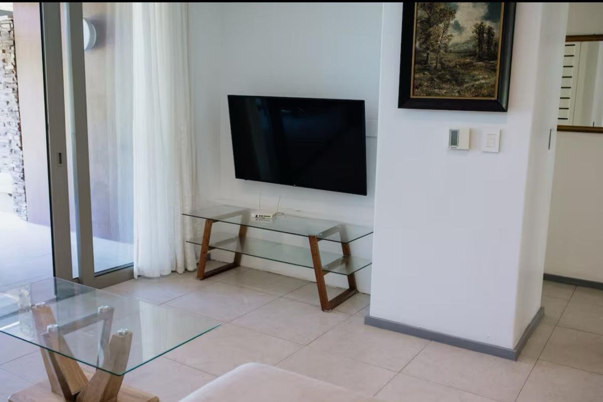 A bright living room featuring tiled flooring, a wall-mounted television, and a large sliding glass door providing access to the outdoor area.