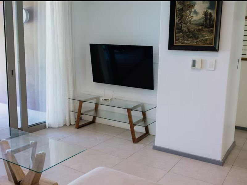 A bright living room featuring tiled flooring, a wall-mounted television, and a large sliding glass door providing access to the outdoor area.