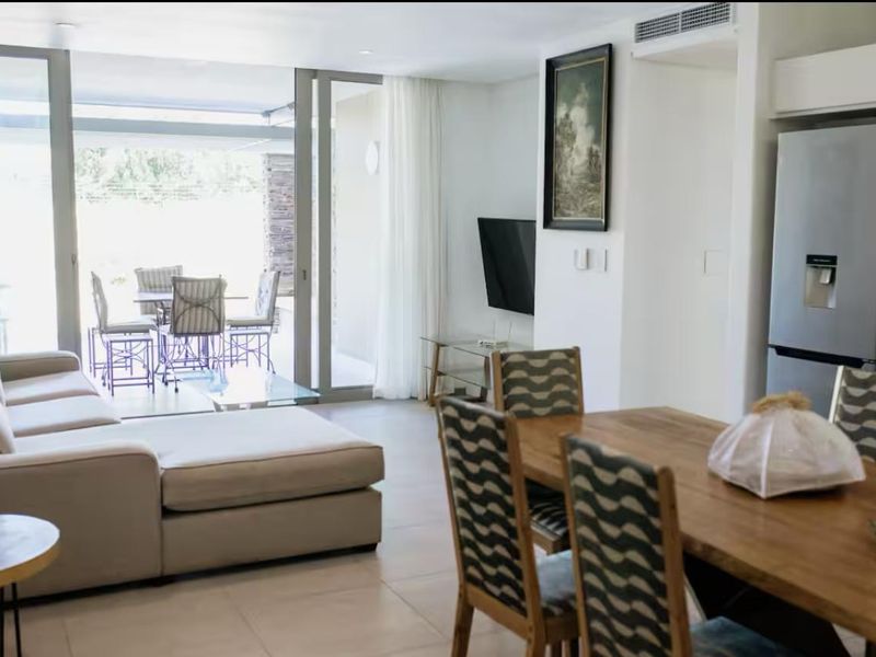 Modern open-plan living and dining area featuring large sliding glass doors that open onto a patio, with neutral tiled flooring and integrated air conditioning.