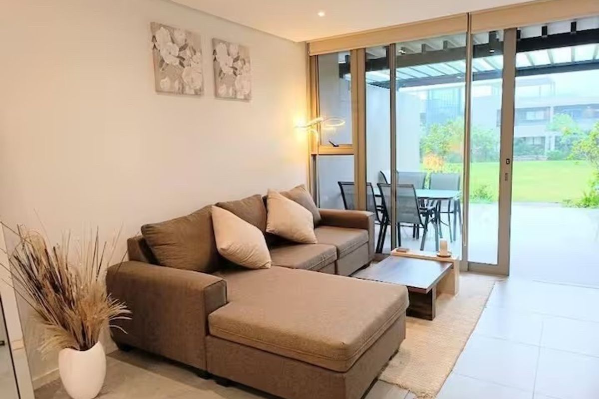 A bright living room featuring large sliding glass doors that open onto a patio, with neutral tiled flooring and modern recessed lighting.