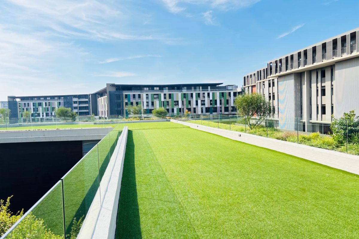 A well-maintained rooftop garden area featuring artificial turf and modern glass balustrades, overlooking the surrounding apartment complex.