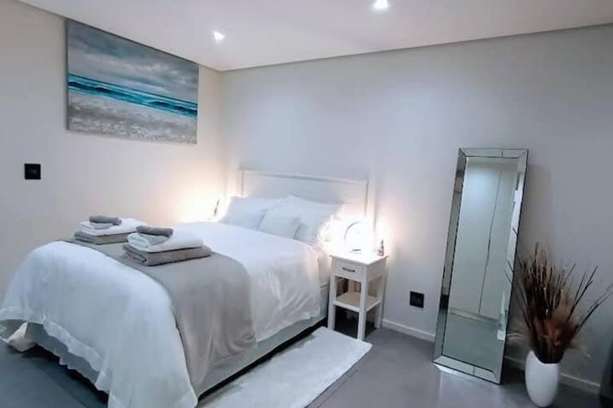 A modern, well-maintained bedroom featuring neutral tones, tiled flooring, recessed downlighting, and built-in storage cupboards.