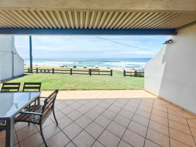 A covered patio featuring tiled flooring and a corrugated metal roof, offering direct access to a lawn area with scenic ocean views.