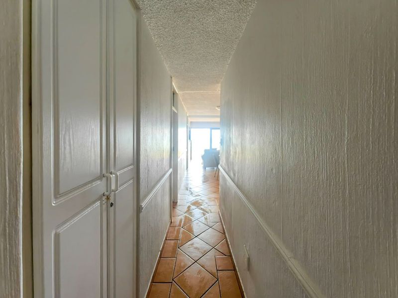 A narrow hallway featuring built-in storage cupboards, textured ceilings, and ceramic tile flooring leading towards an open living area.