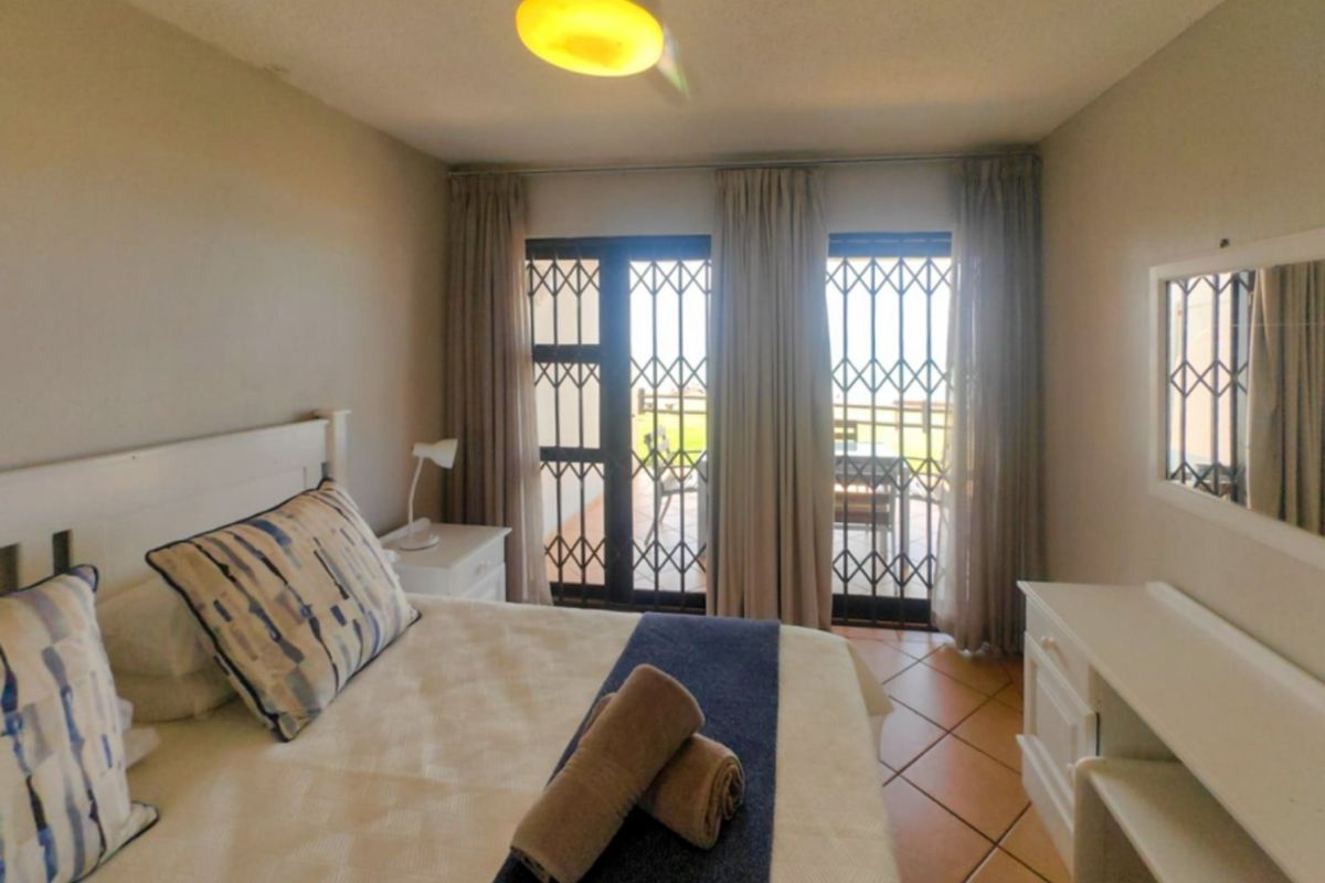 A bedroom featuring tiled flooring, a ceiling fan, and sliding glass doors with security gates leading to an outdoor patio area.