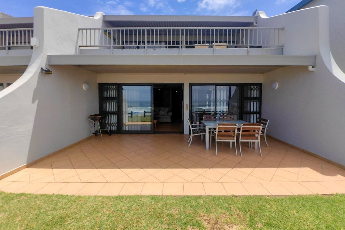 A ground-floor patio area featuring tiled flooring, sliding glass doors with security gates, and an overhead balcony with metal railings.