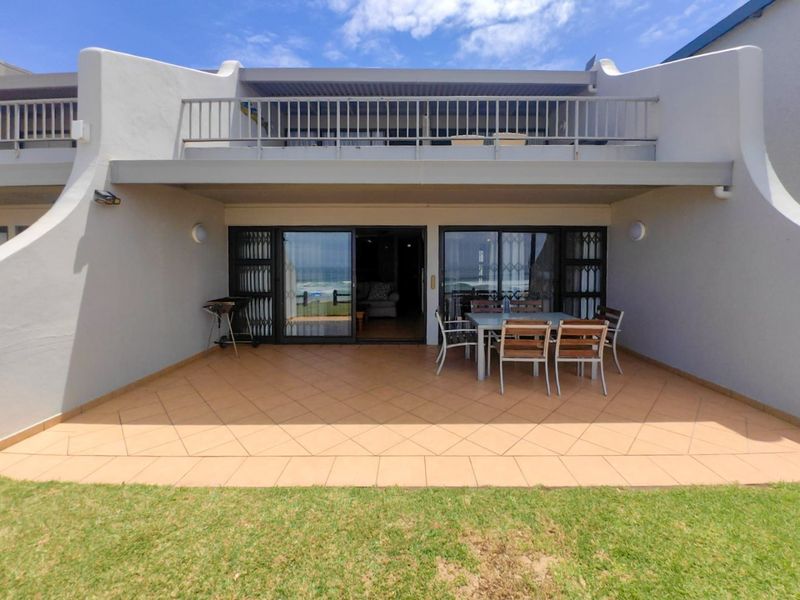 A ground-floor patio area featuring tiled flooring, sliding glass doors with security gates, and an overhead balcony with metal railings.