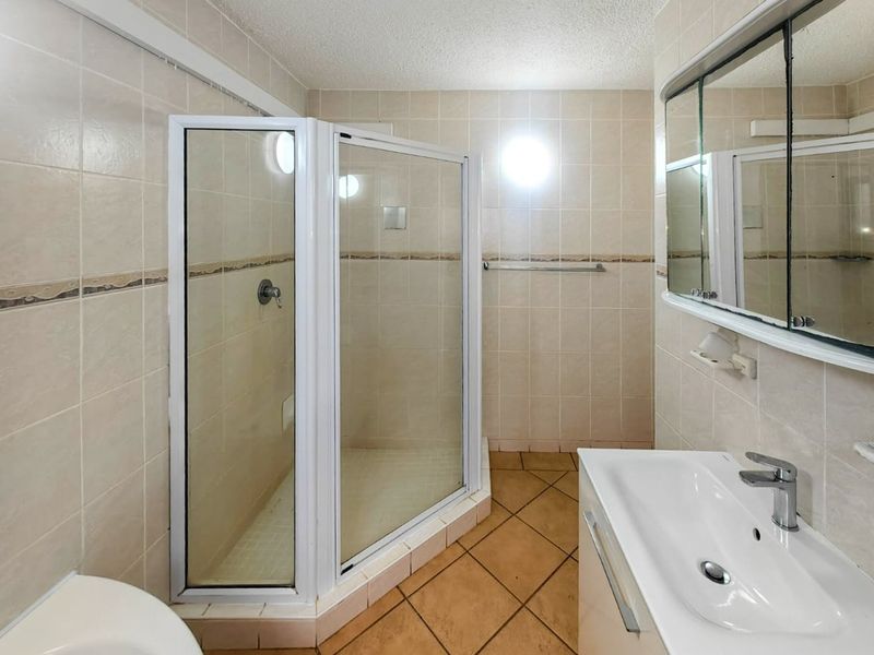 A functional bathroom featuring a corner shower enclosure, vanity basin with integrated storage, and neutral wall and floor tiling.