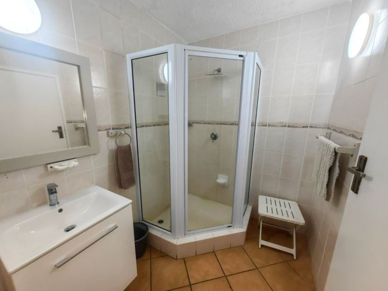 A functional bathroom featuring a corner shower enclosure, vanity basin with storage, and neutral wall tiling throughout.