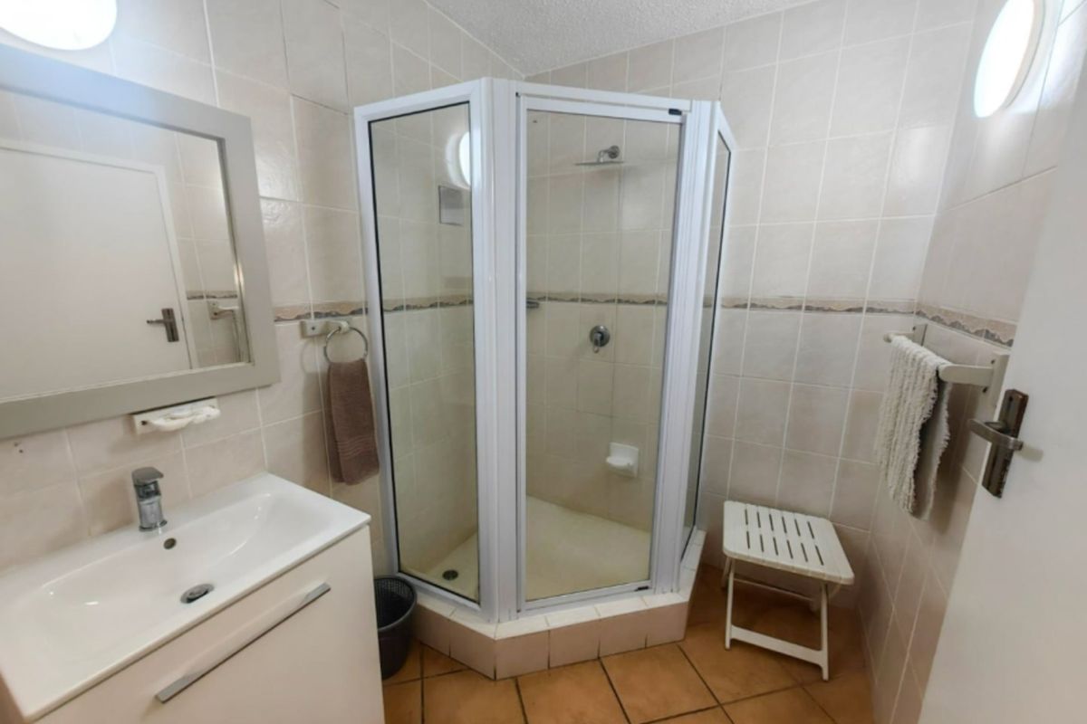 A functional bathroom featuring a corner shower enclosure, vanity basin with storage, and neutral wall tiling throughout.