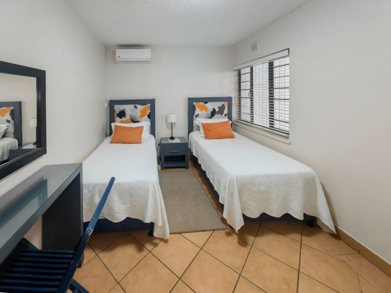 A functional bedroom featuring tiled flooring, a wall-mounted air conditioning unit, and security bars on the window.