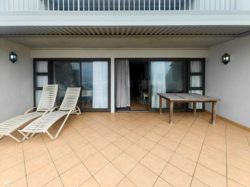 A covered balcony featuring tiled flooring and sliding glass doors, providing a functional outdoor space for relaxation.