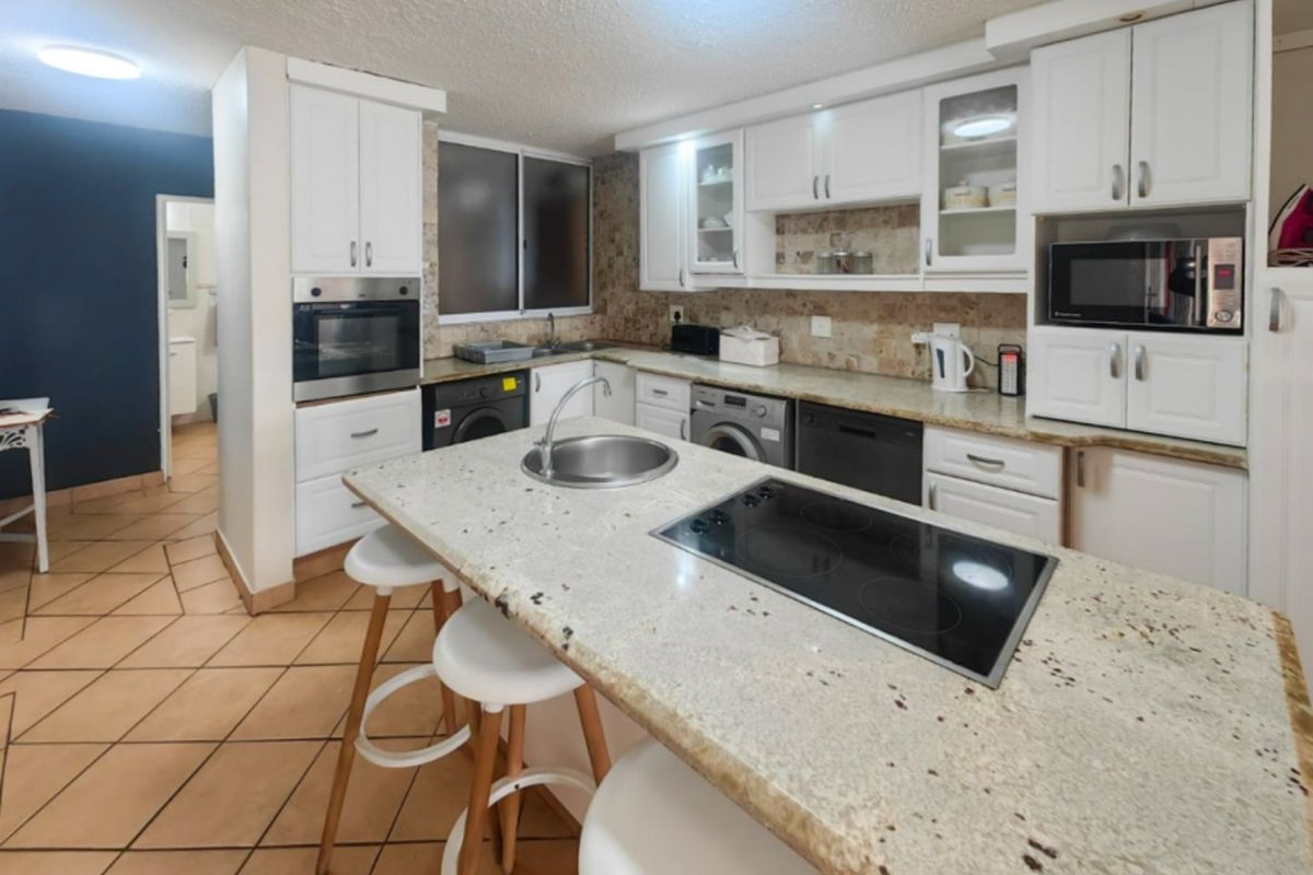 A functional kitchen featuring white cabinetry, granite countertops, a central island with a built-in cooktop, and integrated appliances including an oven and microwave.