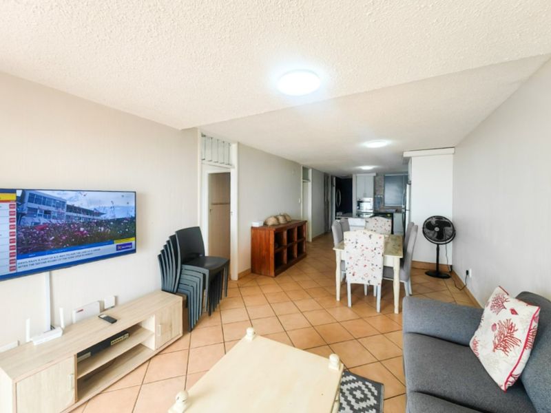 Open-plan living and dining area featuring ceramic tile flooring and a functional kitchen layout, offering a versatile space for modern apartment living.