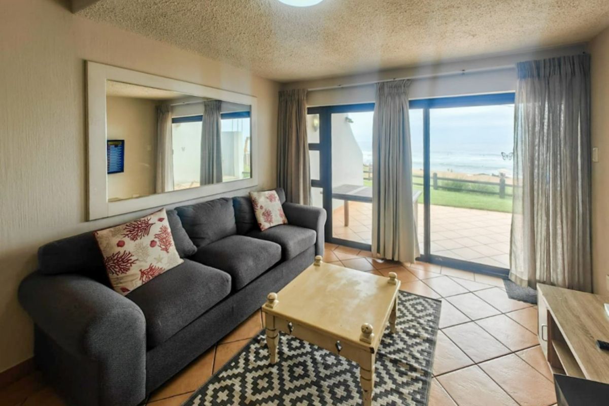 A comfortable living room featuring ceramic floor tiles and large sliding glass doors that provide direct access to an outdoor patio with ocean views.