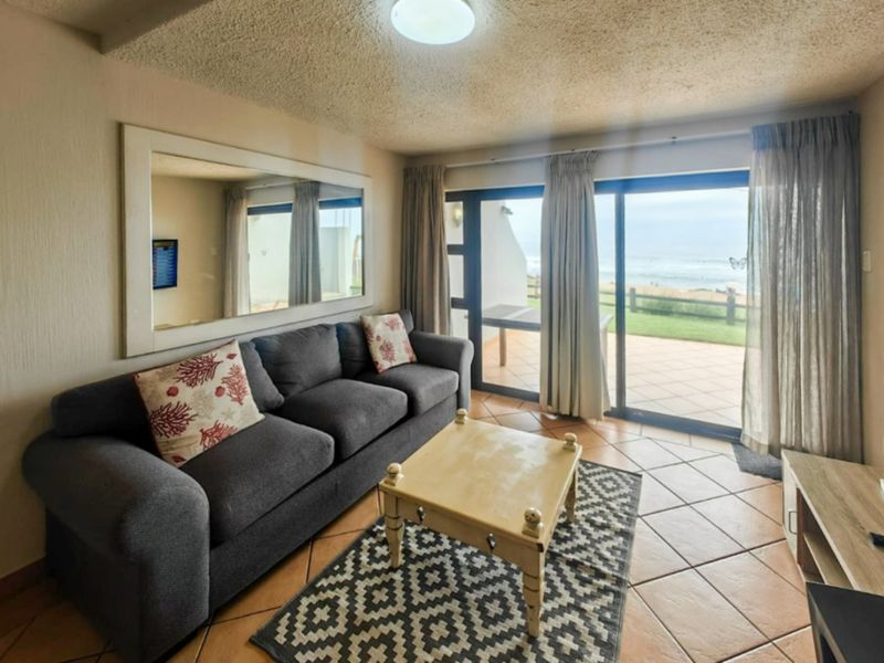 A comfortable living room featuring ceramic floor tiles and large sliding glass doors that provide direct access to an outdoor patio with ocean views.