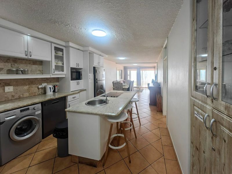 Open-plan kitchen and living area featuring a central island with granite countertops, tiled flooring, and ample built-in cabinetry.